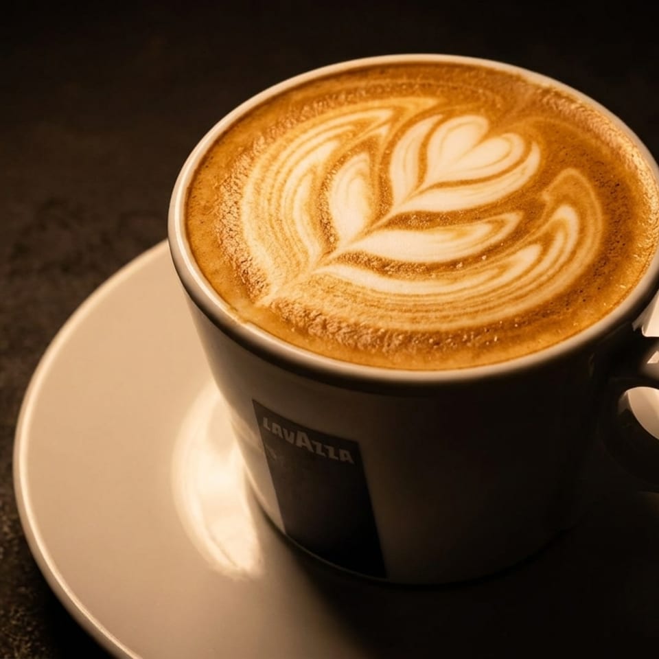 A Lavazza coffee cup with latte art, featuring a heart and leaf design, on a dark surface.