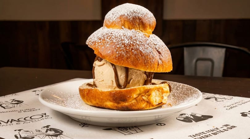 Brioche bun with a scoop of ice cream and chocolate drizzle, dusted with powdered sugar.